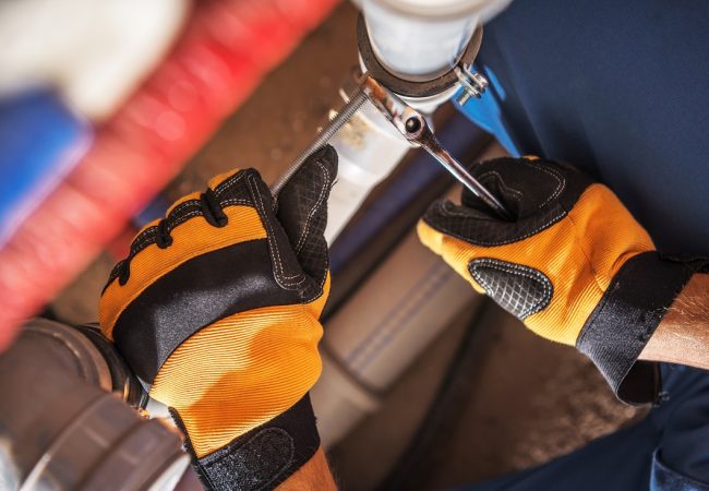 Caucasian Plumber Worker Wearing Safety Gloves Adjusting Water and Sewage Residential System Elements.